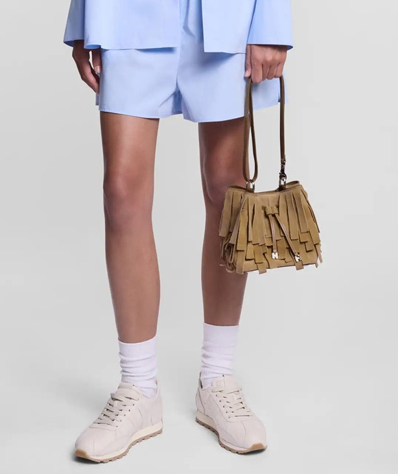 image d'une femme portant un sac à main à franges, un short et une chemise bleu ainsi qu'une paire de baskets beiges